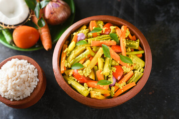 Aviyal and rice Kerala mixed vegetable curry with grated coconut on dark black background in terracotta or clay pot Kerala, Tamil Nadu in South India. Top view Indian veg festival food Onam Sadhya.