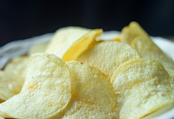A close-up shot of crispy potato chips or salted chips as snacks or junk food on a black background.