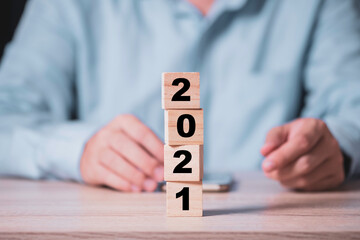 Businessman flipping wooden cubes block to change 2020 to 2021 year on wooden table. Happy new year...