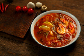 Tom yam soup with shrimp and lime in a light plate on the table ginger, lime and mushrooms.