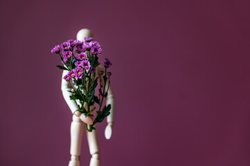 Fototapeta premium Wooden mannequin is holding tiny purple flowers like chrysanthemum, concept of giving flower bouquet to lady