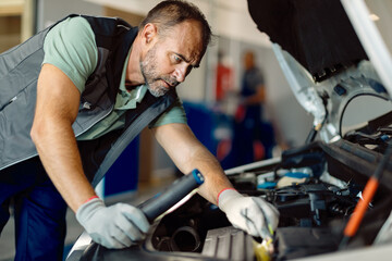 Fototapeta na wymiar Car mechanic examining engine problems while working in repair shop.