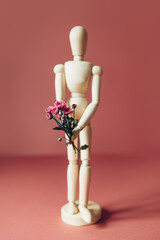 Wooden mannequin is holding tiny purple flowers like chrysanthemum, concept of giving flower...