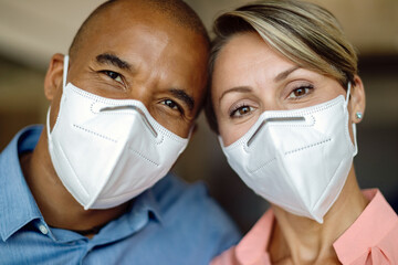 Close-up of happy multi-ethnic couple with protective face masks looking at camera.