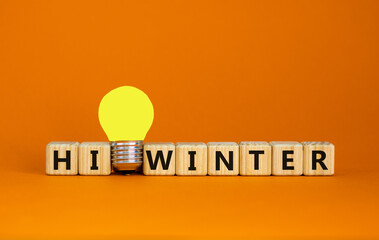 Wooden cubes with words 'hi winter'. Yellow light bulb. Beautiful orange background. Business concept. Copy space.