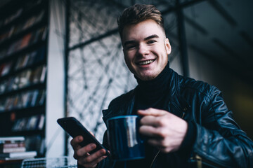 Joyful man enjoying coffee and browsing smartphone