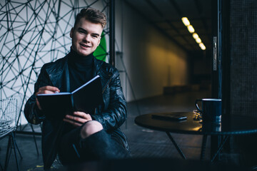 Cheerful young male student preparing for exam in modern cafe
