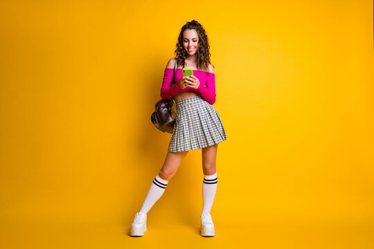 Full length photo of cute lovely lady hold telephone typing wear rucksack pink top uncovered shoulders mini skirt stockings sneakers isolated yellow color background