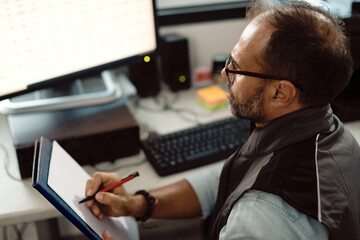 Auto repairman writing notes while working on a computer in the office.