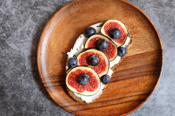 One sandwich with figs, cheese, honey and nuts on a wooden plate decorated with blueberries. Homemade. Casual autumn kitchen. The concept of healthy eating.