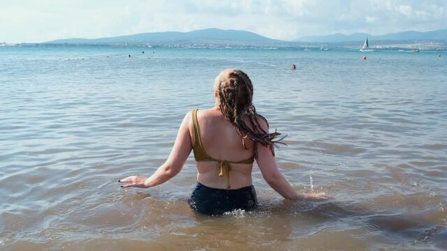 Young woman takes dip in sea. Concept. Woman on vacation swimming in sea with muddy water. Woman swims in sea on background of sailing ships and mountains. Vacation at sea