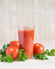 Fresh tomato juice in glass with parsley and ripe tomatoes on light wooden table. Selective focus