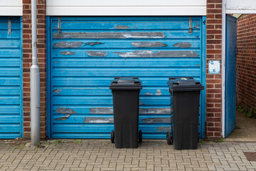 Naklejka premium Two black wheelie bins outside the garage of a home awaiting collection