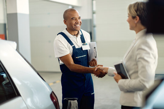 Happy African American mechanic handshaking with businesswoman in auto repair shop.