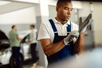 Fototapeta na wymiar Black auto mechanic putting on protective gloves at repair shop.
