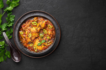 A Chicken Patiala in black bowl on dark slate table top. Murg Patiala is indian cuisine curry dish with chicken meat, spices, curd and cashew nut paste. Asian food and meal. Copy space