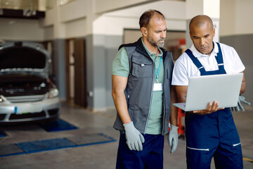 Auto repairmen cooperating while working on laptop at car service workshop.