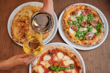 Friends having pizza party dinner. Flat-lay of people cutting and eating Italian pizza and drinking  wine from glasses over wooden table, top view. Fast food lunch, gathering, celebration 