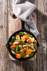Stir fry chicken with vegetables on iron pan on wooden table	