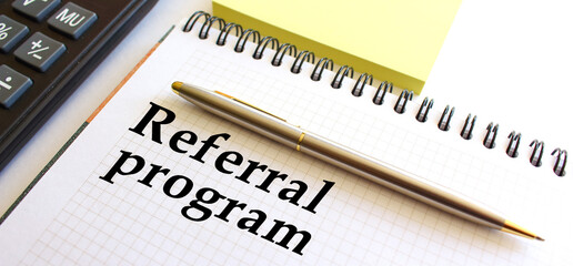 Notepad with text REFERRAL PROGRAM on a white background, near calculator and yellow note papers. Business concept.