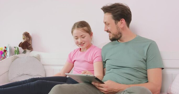 Father and teen daughter sitting on the sofa in living room, browsing the online store, enjoying weekend. Father agrees to choose the thing, his daughter like, and girl is happy about it. And suddenly