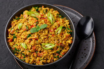 Masala Egg Bhurji or Muttai Podimas in black bowl on dark slate table top. Anda Bhurji is indian cuisine scrambled eggs dish with spices. Asian food and meal.