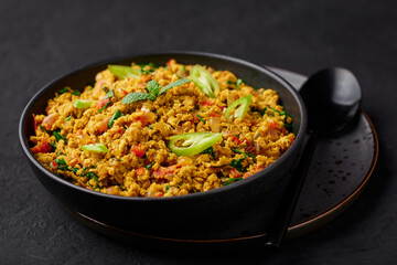 Masala Egg Bhurji or Muttai Podimas in black bowl on dark slate table top. Anda Bhurji is indian cuisine scrambled eggs dish with spices. Asian food and meal.