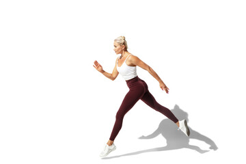 Running. Beautiful young female athlete practicing on white studio background, portrait with shadow. Sportive fit model in motion and action. Body building, healthy lifestyle, style concept.