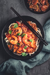 Flat lay of Japanese udon noodles fried with sweet and sour shrimps sauce with hot pepper in Asian style, black dishware, concrete background, dark mood