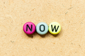 Round color bead with black letter in word now on wood background