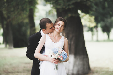 Stylish couple of happy newlyweds walking in the park on their wedding day with bouquet
