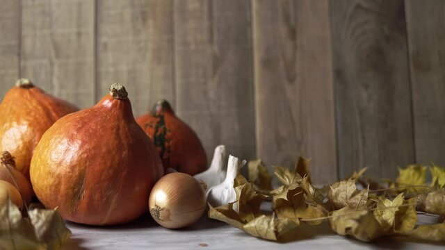 Autumn still-life with vegetables and dry maple foliage. Concept of rural decoration with raw food. There are orange pumpkins next to garlic and onions on board. Fall composition on wooden background.