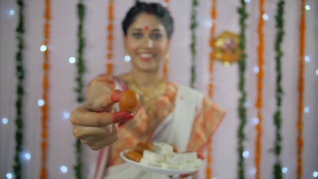 A young Bong Beauty offering a famous Bengali sweet during the festival - Durga Puja. Medium shot of a Bengali lady wearing a traditional saree giving famous sweet (Pantua) to her friends - Indian ...
