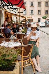 beautiful stylish young woman in a hat sitting at a table in a cafe and drinking coffee