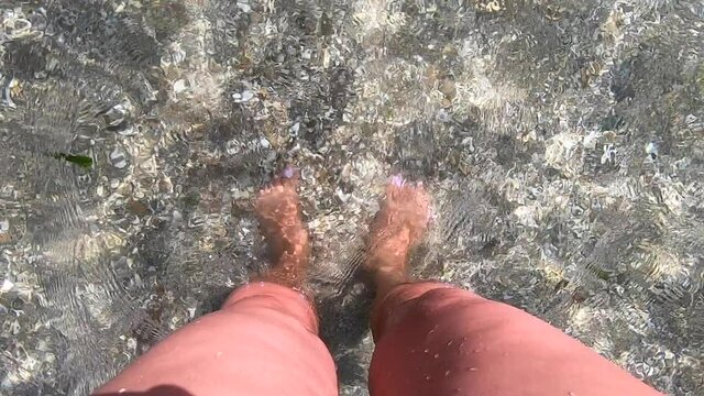 Girl standing knee-deep in water on beach with brown sand and shells