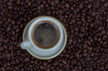 Black coffee in light brown cup on coffee beans background top view