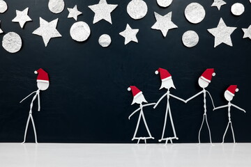 Fototapeta na wymiar Alone man beside a complete family stick figure wearing santa hat in black background with stars and silver christmas ornaments. Solo versus celebrating christmas together concept.
