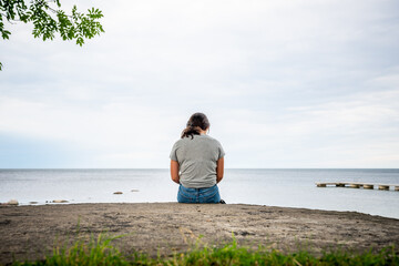 Young girl sitting on a rock looking out on the ocean. Nature view with rock, water and horizon in the background.