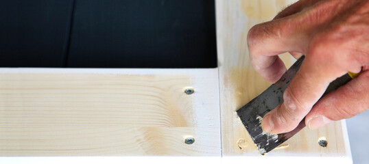 Putty knife in man's hand. DIY worker applying filler to the wood. Removing holes from a wood...