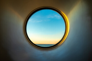 Sunset ocean view of horizon seen from inside of a cruise ship cabin through a round circular window.