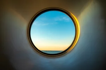 Fotobehang Sunset ocean view of horizon seen from inside of a cruise ship cabin through a round circular window. © Pebo
