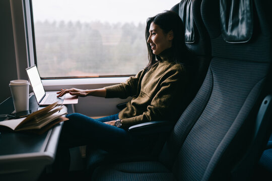 Cheerful asian woman traveler enjoying watching movie on laptop computer in wagon satisfied with wireless connection, smiling 20s female reading news working remotely on business trip in train