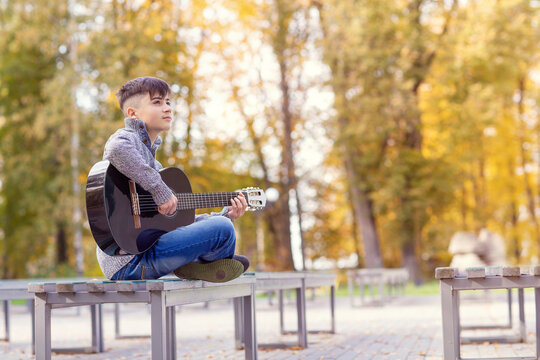 A Teenage Street Musician Plays A Black Acoustic Guitar On An Autumn Day In The Park