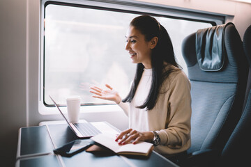 Happy prosperous asian businesswoman smiling during video call connection sitting in wagon on trip, 20s smiling female laughing at funny video on laptop computer traveling by train on journey - obrazy, fototapety, plakaty