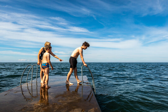 Summer view of a family on a stone jetty about to  swim in the ocean of the Baltic Sea with blue sky and horizon in the background.