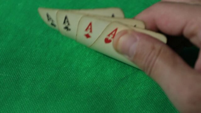 Close up, a man's hand scans his four aces while playing poker.