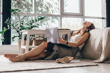 Tired girl is sitting on the floor of the bedroom leaning back on the bed