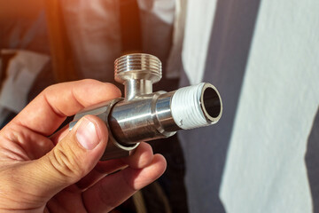 A man holds in his hand a distribution pipeline fitting with a shut-off valve for water supply. Details of the pipeline.Connect the pipe to the tap.Installation of the crane on the pipe. Close-up.