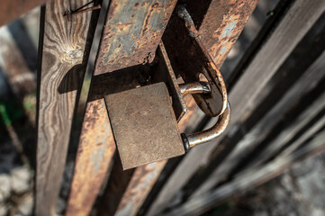 Rusty padlock hanging on wooden rural gate outdoors. View from above. Locked gates, locked doors, closed area, restricted passage, private property.
