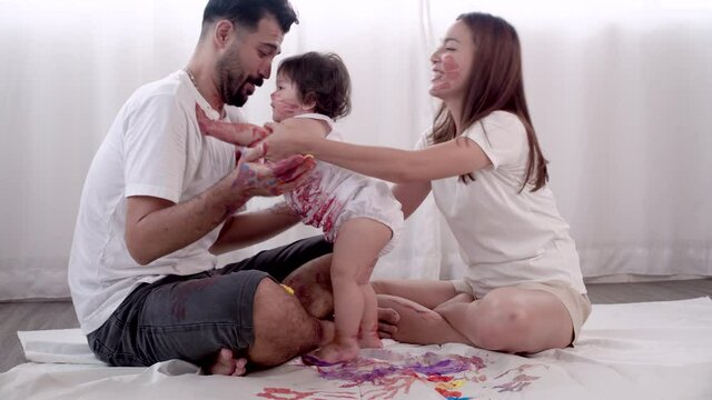 Joyful family rest playful funny at home. Enjoyment daughter playing color and holding hand color with her parent together in the room. Mixed race kid and parenthood concept.